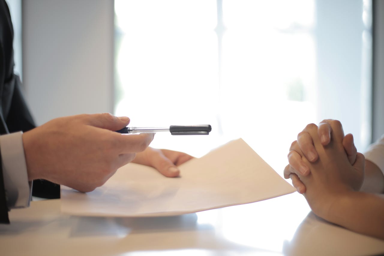 gallery-5 Side view of faceless formal man giving pen and paper to focused female with clenched hands at table on meeting