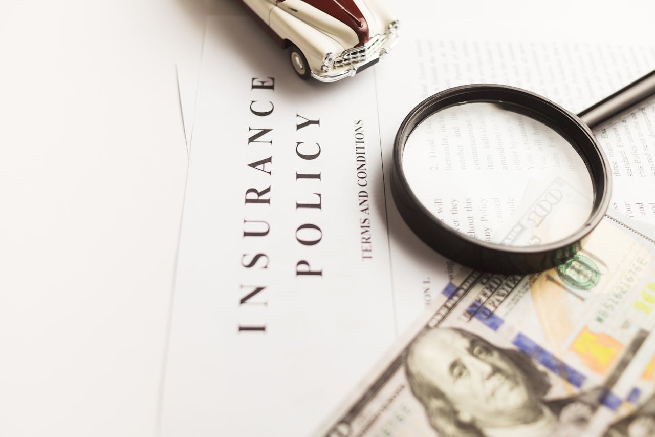 gallery-6 Close-up image of an insurance policy with a magnifying glass, money, and toy car.