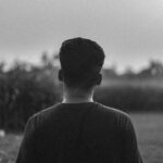 Black and white image of a man standing in a field, thoughtful mood captured from behind.